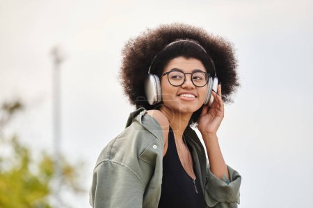 Eine stylische junge Frau genießt Musik in ihren Kopfhörern, während sie eine trendige Jacke trägt.