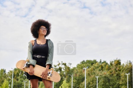 Energetische junge Afroamerikanerin mit lockigem Haar hält selbstbewusst ein Skateboard in einem lebhaften Outdoor-Skatepark.