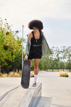 A young African American woman with curly hair exudes style as she gracefully holds a skateboard in a black dress at a skate park.
