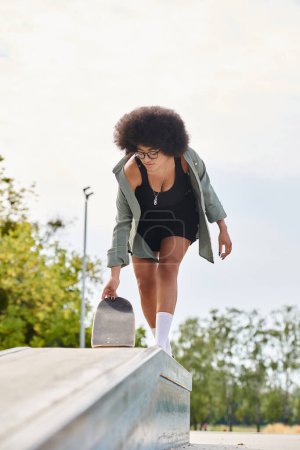 A young African American woman with curly hair glides on a skateboard in a skate park.