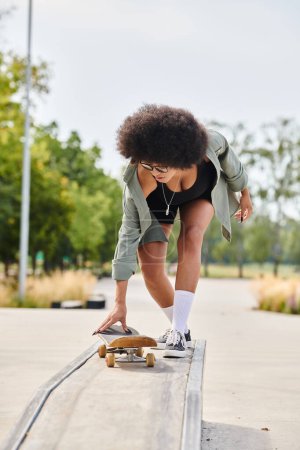 A young African American woman with curly hair confidently skateboarding down a metal rail at an outdoor skate park.