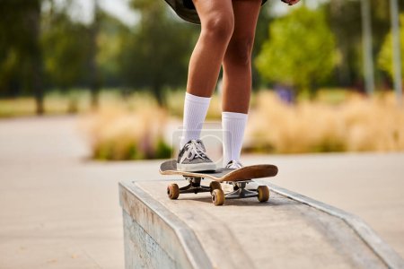 Eine junge Afroamerikanerin führt in einem städtischen Skatepark einen gewagten Skateboard-Trick auf einem Sims vor.