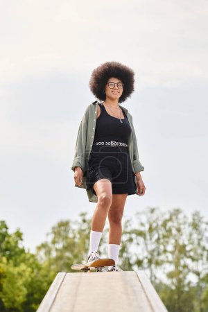 A young African American woman with an afro is skateboarding gracefully on a ramp in an outdoor skate park.