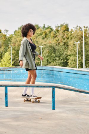 Young African American woman with curly hair rides a skateboard fearlessly on a metal rail at an outdoor skate park.