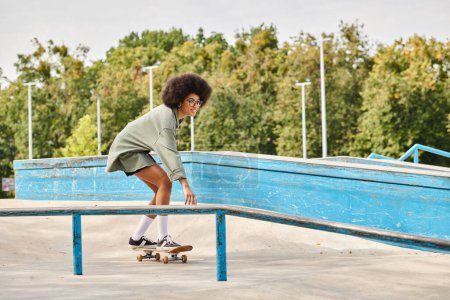 A young African American woman with curly hair skillfully rides a skateboard on a rail in an outdoor skate park.