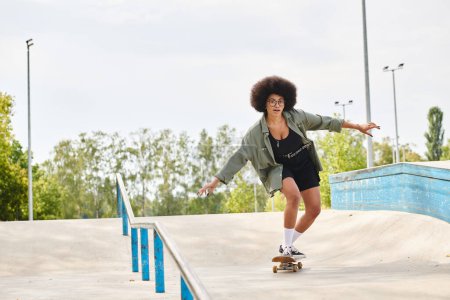 Photo for A young African American woman with curly hair confidently rides a skateboard down the side of a ramp at an outdoor skate park. - Royalty Free Image