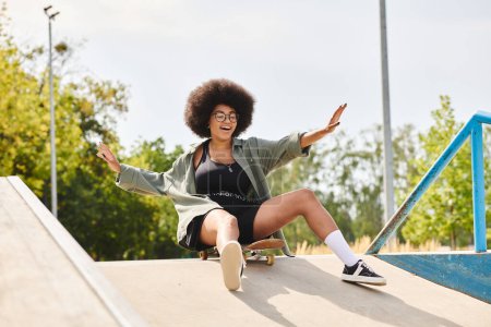 Foto de Una joven afroamericana con el pelo rizado monta un monopatín al lado de una rampa en un parque de skate al aire libre. - Imagen libre de derechos