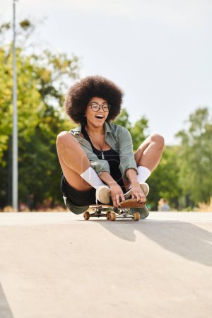 Young African American woman with curly hair confidently sits on top of a skateboard as she conquers a steep ramp at the skate park.