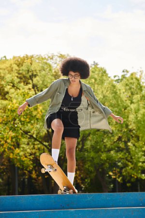 A young African American woman with curly hair skillfully skateboarding on top of a blue ramp in an outdoor skate park.