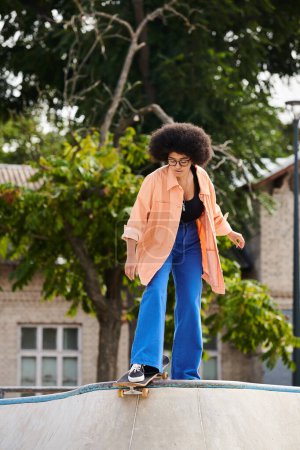 Foto de Una joven afroamericana con el pelo rizado monta hábilmente un monopatín en una rampa en un parque de skate al aire libre. - Imagen libre de derechos