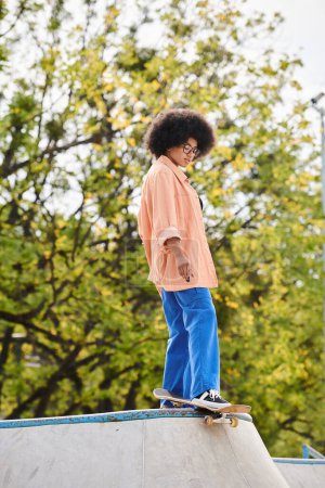 A curly-haired young man confidently rides a skateboard on top of a cement ramp in a skate park.