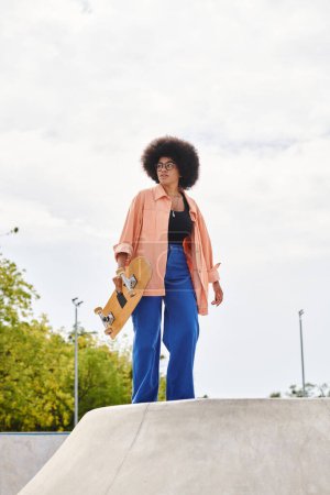 A young African American woman with a curly afro hairdo confidently holds a skateboard at an outdoor skate park.