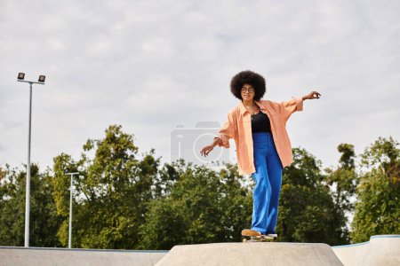 Photo for Young African American woman with curly hair skateboarding on top of a cement ramp in a skate park. - Royalty Free Image