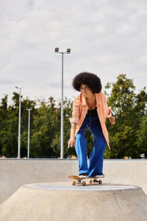A young African American woman with curly hair rides a skateboard on top of a cement ramp in an urban skate park.