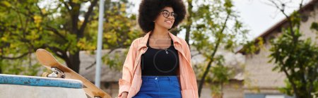 Téléchargez les photos : Une jeune afro-américaine aux cheveux bouclés se tient à côté d'une planche à roulettes dans un parc, prête à frapper les rampes et à montrer ses compétences. - en image libre de droit