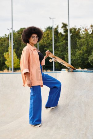 A young African American woman with curly hair skillfully standing on top of a skateboard ramp in an outdoor skate park.
