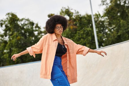 Foto de Una joven afroamericana con el pelo rizado monta con confianza su monopatín al lado de una rampa en un parque de skate al aire libre. - Imagen libre de derechos