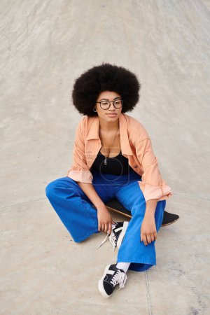 Photo for A young African American woman with an afro sitting on a skateboard at a vibrant outdoor skatepark. - Royalty Free Image