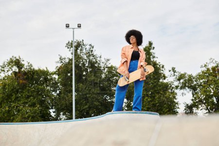 Eine junge Afroamerikanerin mit lockigem Haar steht selbstbewusst auf einer Skateboardrampe in einem Outdoor-Skatepark.