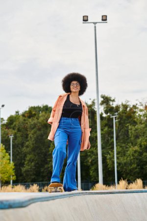 An African American woman with curly hair skateboarding on top of a ramp at an outdoor skate park.
