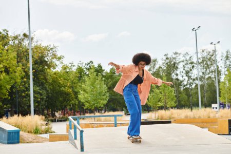 Joven mujer afroamericana con el pelo rizado monta hábilmente un monopatín en una rampa en un parque de skate al aire libre.