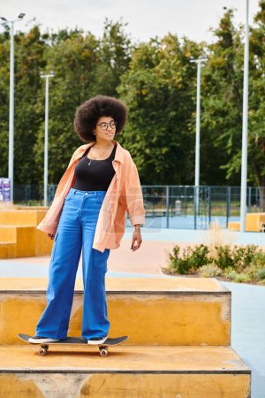 A young African American woman with curly hair confidently stands atop a skateboard ramp in an outdoor skate park.