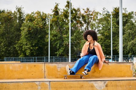 Eine junge Afroamerikanerin mit lockigem Haar sitzt selbstbewusst mit ihrem Skateboard auf einem Sims in einem lebhaften Skatepark.