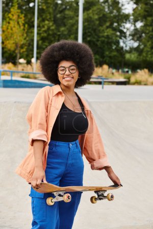 A young African American woman with an afro holding a skateboard at a skate park.