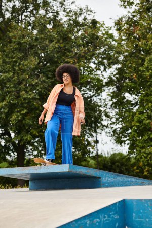 A young African American woman with curly hair gracefully stands on top of a blue object in a skate park.