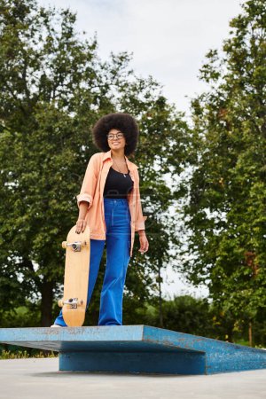 Mujer afroamericana joven con el pelo rizado sosteniendo un monopatín en la parte superior de una plataforma azul en un parque de skate.