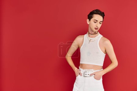 Photo for Stylish appealing gay man in casual attire with accessories posing on red backdrop and looking away - Royalty Free Image
