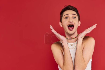 Photo for Cheerful handsome gay man with stylish accessories in white attire looking at camera on red backdrop - Royalty Free Image