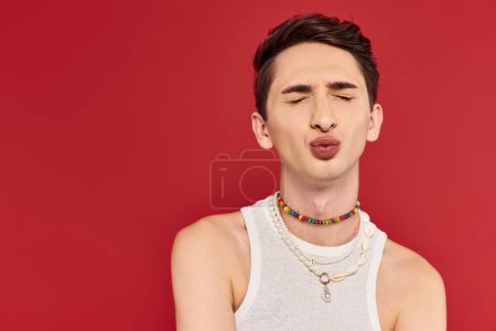 ansprechender junger schwuler Mann in stilvoller weißer Kleidung mit geschlossenen Augen und gestampften Lippen auf rotem Hintergrund