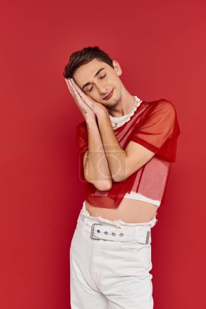 alluring androgynous man in white attire with red fishnet posing with closed eyes like sleeping