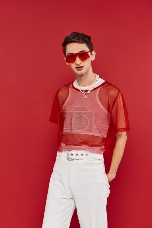 modischer modisch androgyner Mann mit rotem stylischem Fischnetz und Sonnenbrille, der in die Kamera blickt