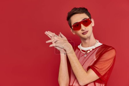 well-dressed androgynous man with red stylish fishnet and sunglasses posing and looking away