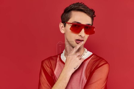 good looking modish androgynous man with red stylish fishnet and sunglasses looking at camera