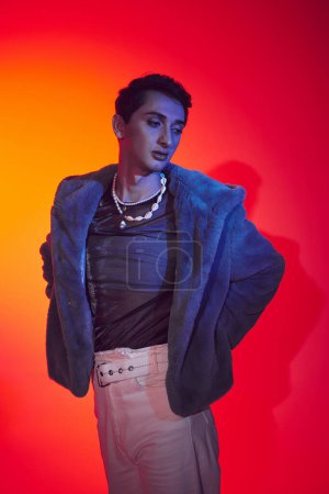 Photo for Alluring modish androgynous man in purple faux fur posing on vibrant backdrop and looking away - Royalty Free Image