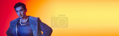Téléchargez les photos : Élégant homme androgyne en fausse fourrure violette posant sur fond vibrant et regardant la caméra, bannière - en image libre de droit