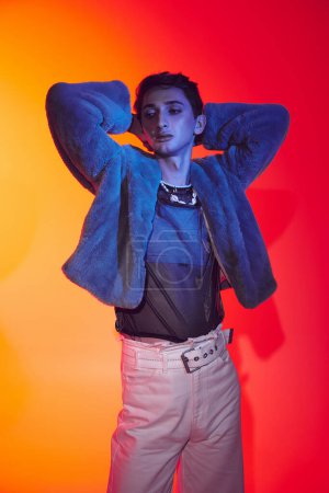 Photo for Appealing modish androgynous man in purple faux fur posing on vibrant backdrop and looking away - Royalty Free Image