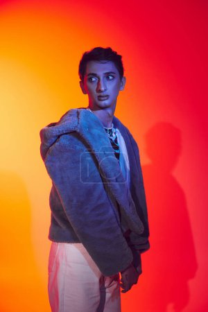 Photo for Good looking modish androgynous man in purple faux fur posing on vibrant backdrop and looking away - Royalty Free Image