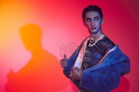 Photo for Handsome modish androgynous man in purple faux fur posing on vibrant backdrop and looking away - Royalty Free Image