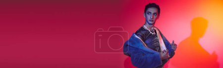 stylish androgynous man in purple faux fur posing on vibrant backdrop and looking away, banner