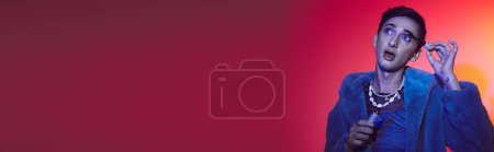 Téléchargez les photos : Bel homme androgyne en fausse fourrure violette à l'aide de mascara sur fond vibrant, bannière - en image libre de droit