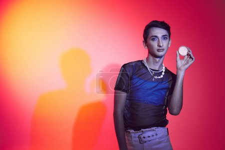 Photo for Good looking stylish gay man in casual vivid attire holding cream in his hands and looking at camera - Royalty Free Image