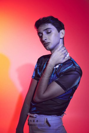 Photo for Young modish androgynous man in casual vivid attire posing with closed eyes on vibrant backdrop - Royalty Free Image
