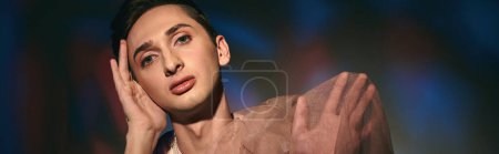 Photo for Chic androgynous man with dark hair in pastel attire looking at camera on vivid backdrop, banner - Royalty Free Image