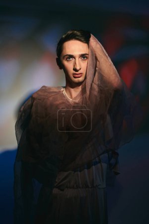Foto de Bien vestido andrógino fashionista en vestido de pastel mirando a la cámara en el vibrante telón de fondo - Imagen libre de derechos