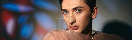 Photo for Cool androgynous man with dark hair in pastel attire looking at camera on vivid backdrop, banner - Royalty Free Image