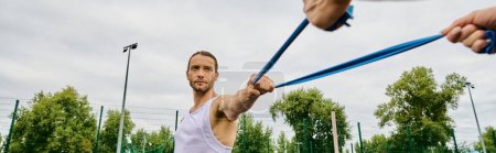 Photo for A man wearing sportswear, holding a blue resistance band outdoors. - Royalty Free Image